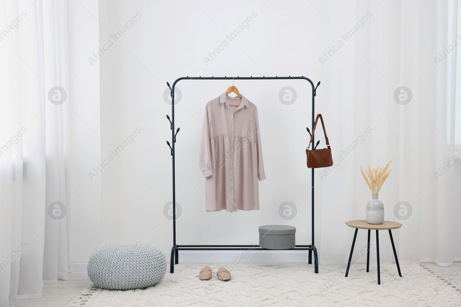 Photo of Clothing rack with stylish dress, bag and shoes in room