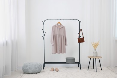 Clothing rack with stylish dress, bag and shoes in room