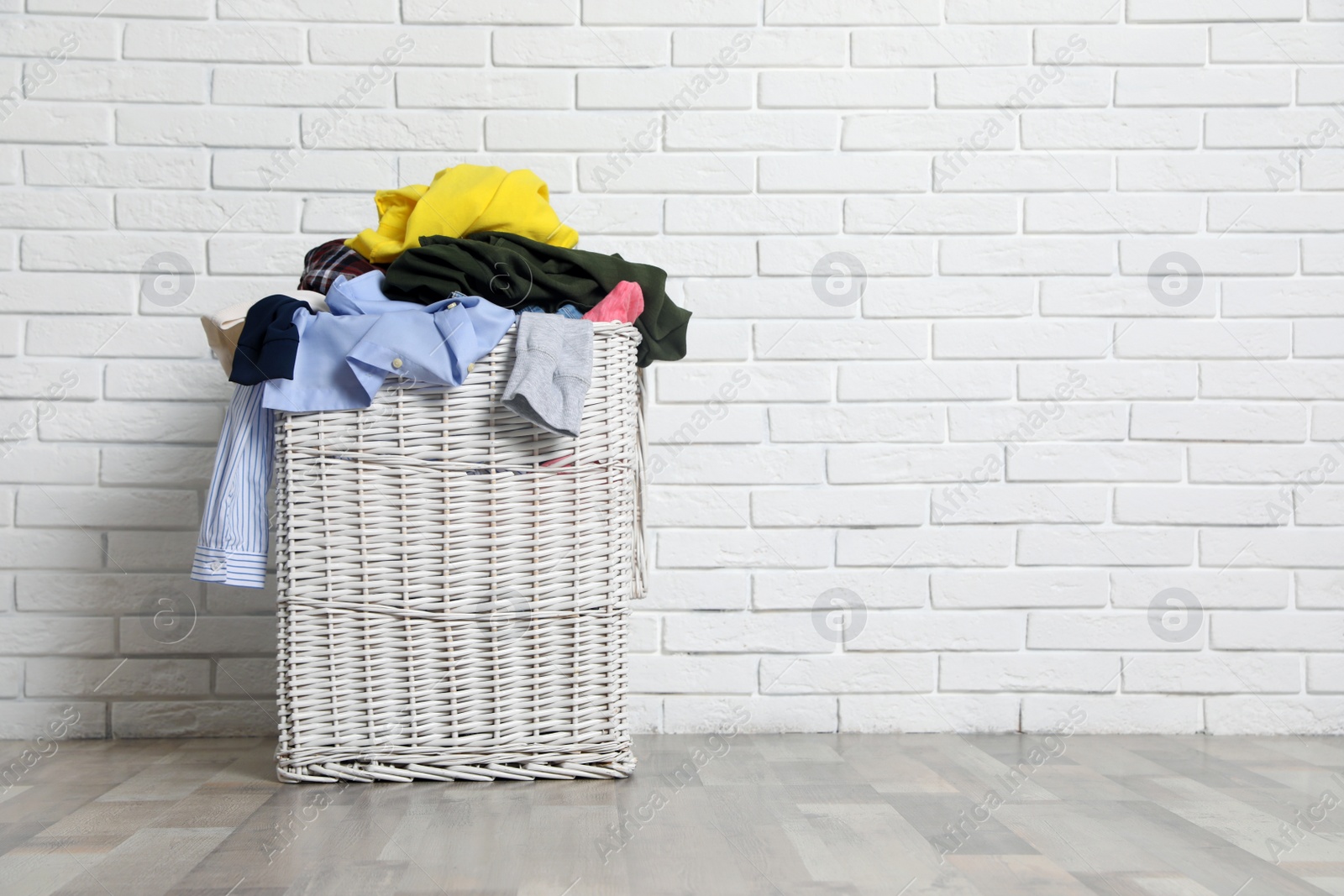 Photo of Laundry basket with dirty clothes on floor near brick wall. Space for text