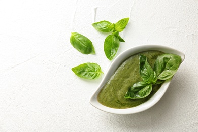 Sauce in gravy boat and basil leaves on white table, top view