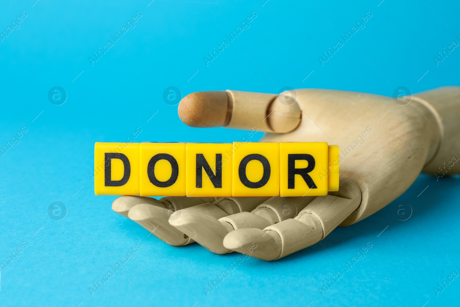 Photo of Mannequin hand holding word Donor made of cubes on light blue background