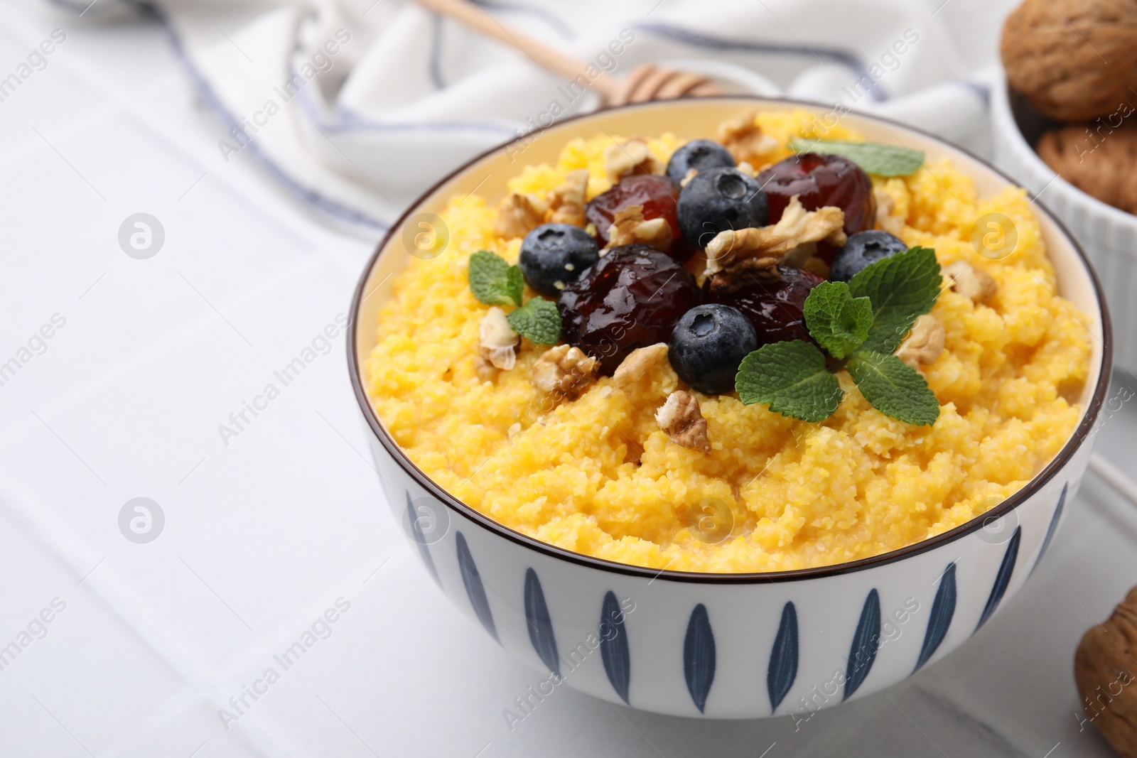 Photo of Tasty cornmeal with blueberries, dates, walnuts and mint in bowl on white table, closeup