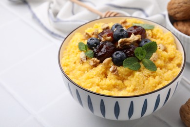 Photo of Tasty cornmeal with blueberries, dates, walnuts and mint in bowl on white table, closeup