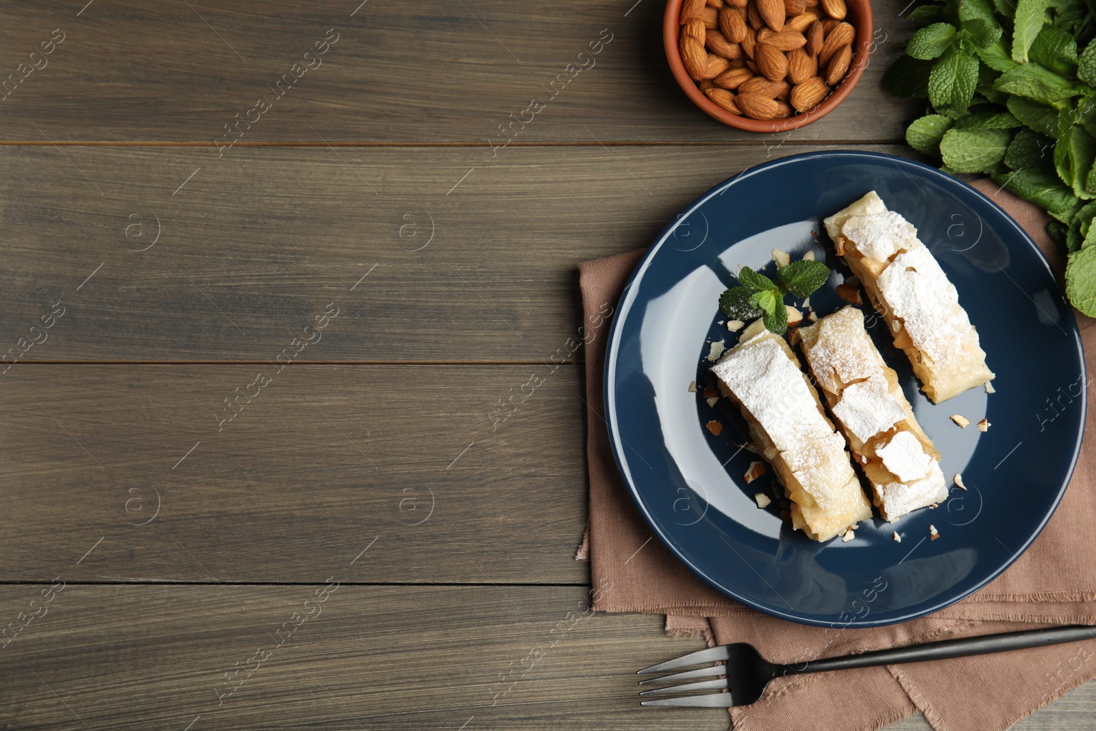 Photo of Delicious apple strudel with almonds, powdered sugar and mint on wooden table, flat lay. Space for text