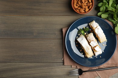 Photo of Delicious apple strudel with almonds, powdered sugar and mint on wooden table, flat lay. Space for text