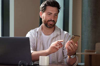 Photo of Handsome man sending message via smartphone at table indoors