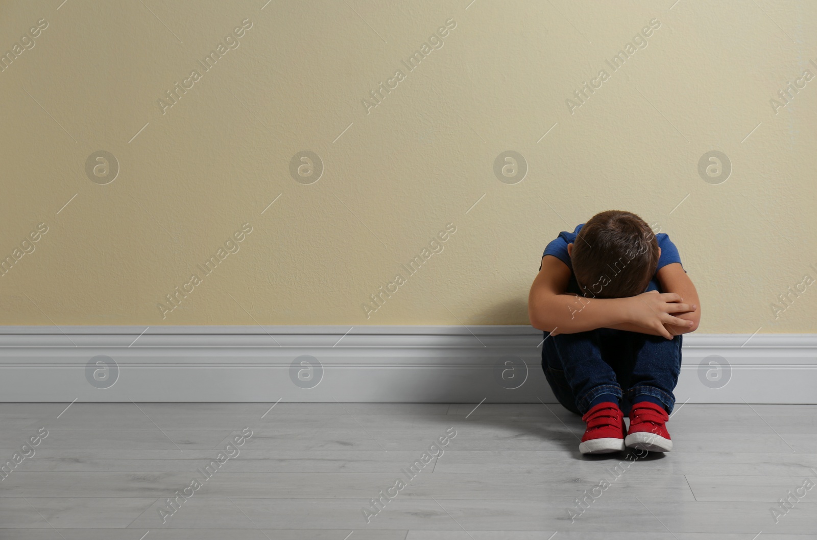 Photo of Little boy on floor near yellow wall, space for text. Child in danger