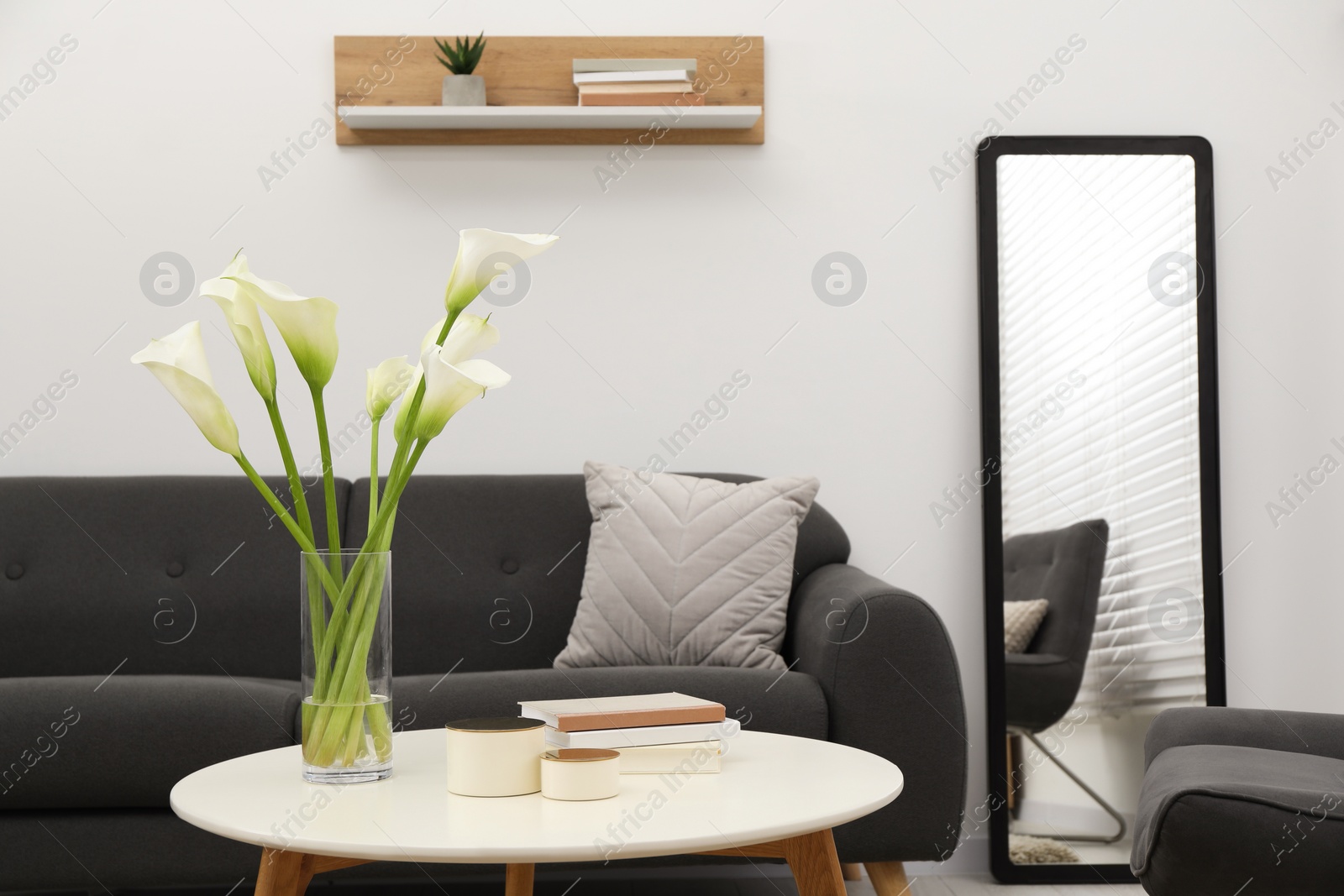 Photo of Beautiful calla lily flowers in glass vase, boxes and books on white table at home