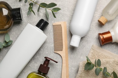 Photo of Shampoo bottles, wooden comb, leaves and towel on grey table, flat lay