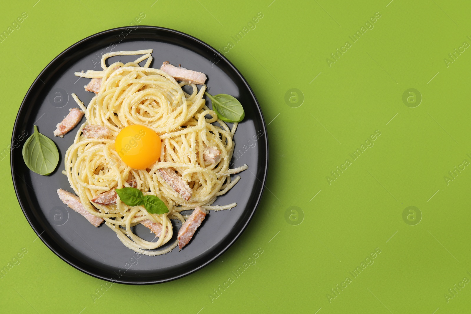 Photo of Plate of tasty pasta Carbonara with basil leaves on light green background, top view. Space for text