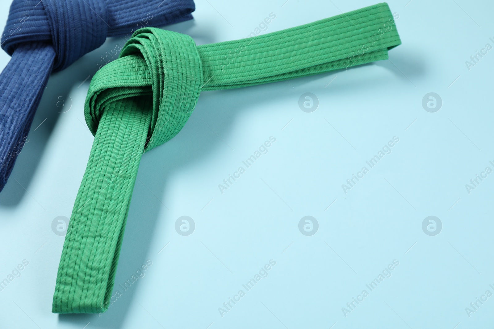 Photo of Colorful karate belts on light blue background, space for text