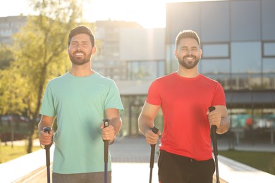 Happy men practicing Nordic walking with poles outdoors on sunny day