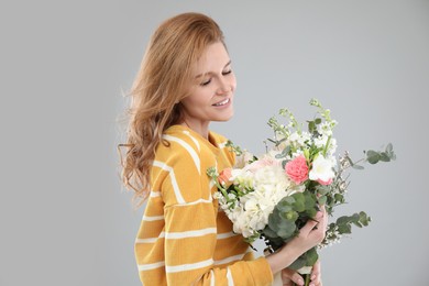 Beautiful woman with bouquet of flowers on grey background