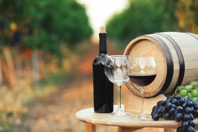 Photo of Bottle of wine, barrel and glasses on wooden table in vineyard