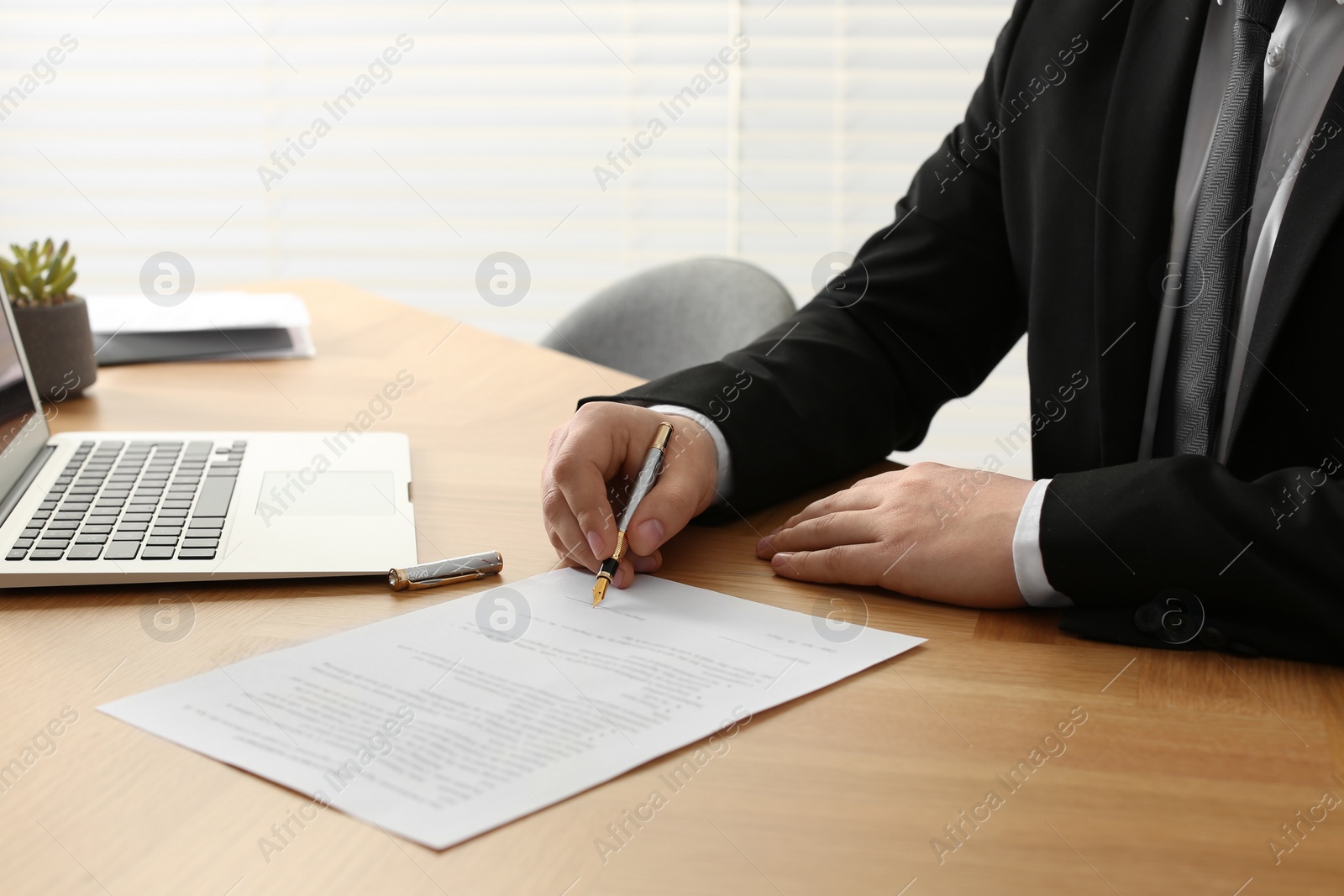 Photo of Notary signing document at wooden table indoors, closeup