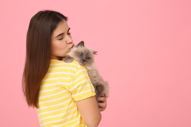 Woman kissing her cute cat on pink background, space for text