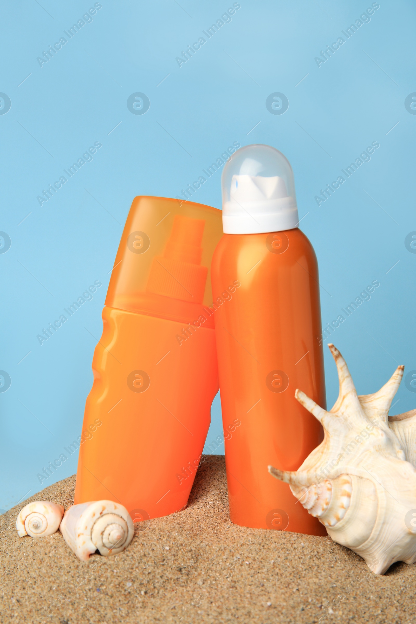 Photo of Sand with bottles of sunscreens and seashells against light blue background. Sun protection