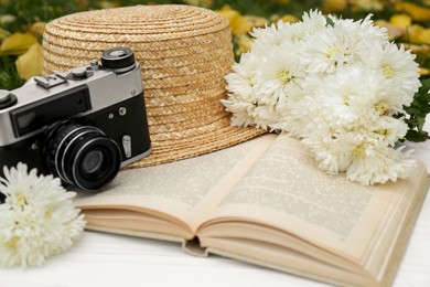 Composition with beautiful chrysanthemum flowers, vintage camera and book on white table outdoors, closeup