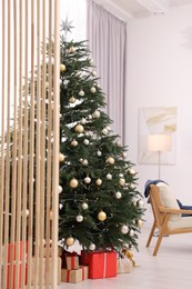 Beautiful Christmas tree with festive lights, gifts and armchair in living room. Interior design