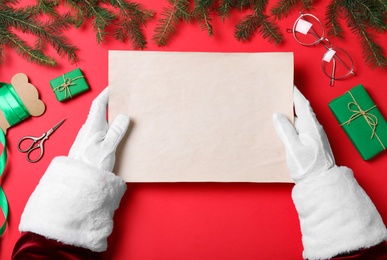 Santa Claus holding empty paper on red background, top view. Space for text