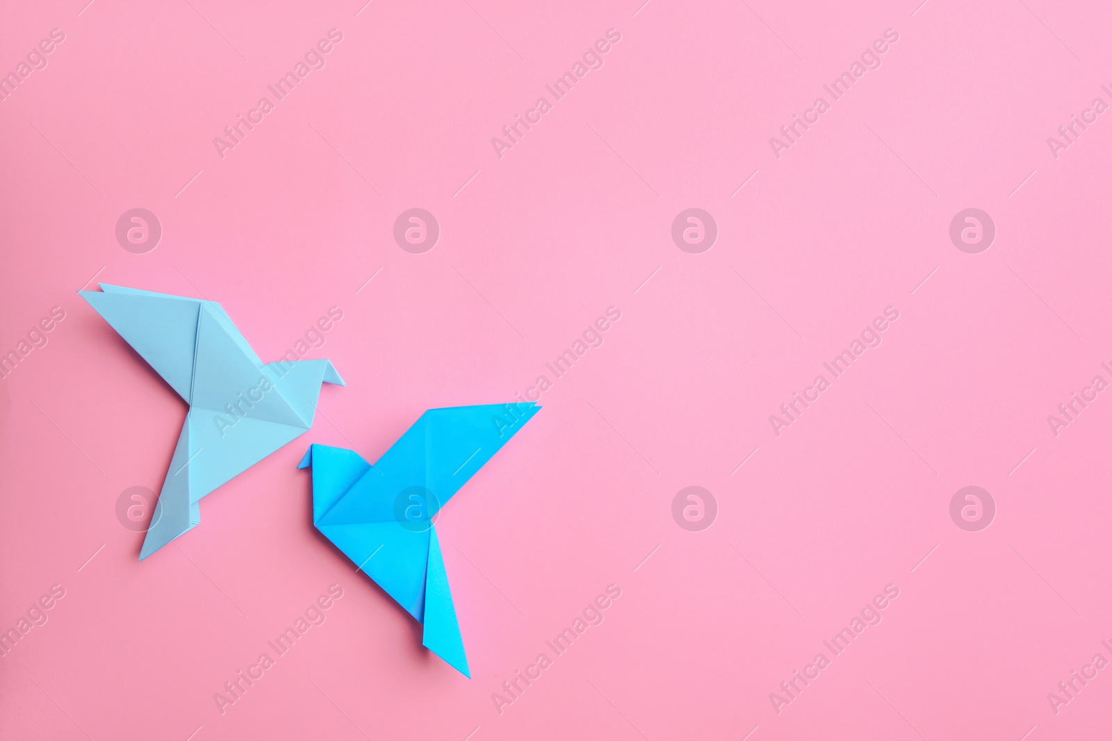 Photo of Beautiful light blue origami birds on pink background, flat lay. Space for text