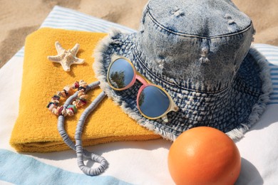 Photo of Denim hat, orange and beach accessories on sand, closeup