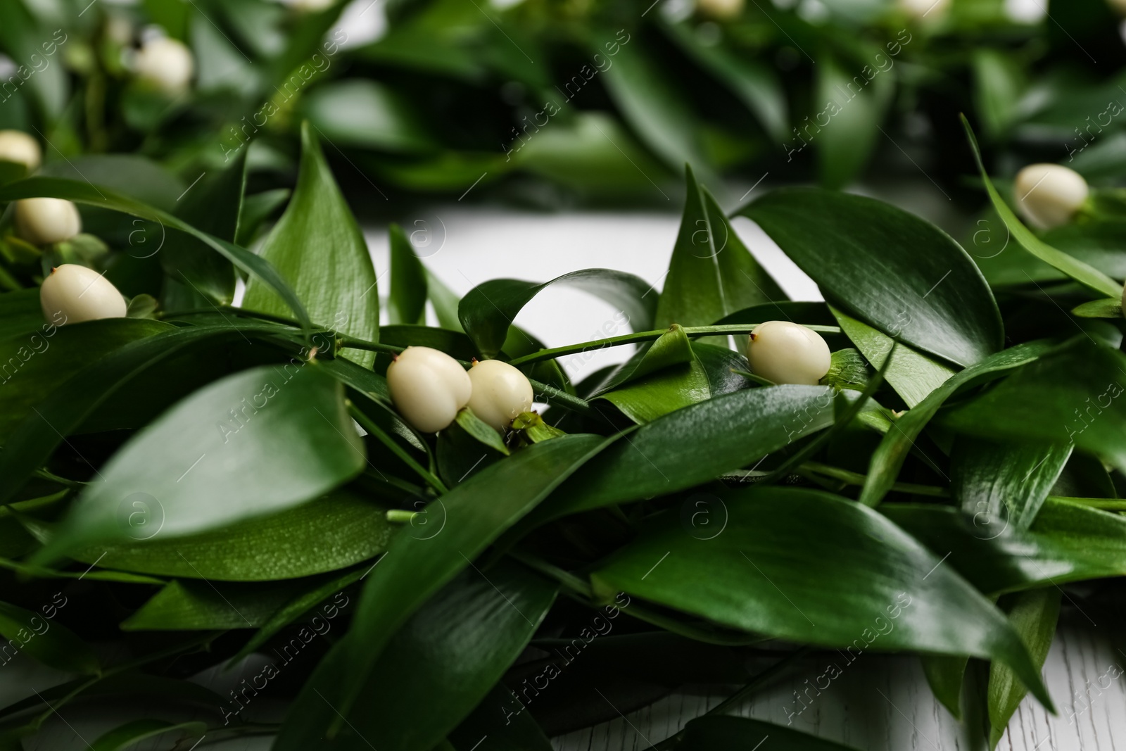 Photo of Beautiful handmade mistletoe wreath on white table, closeup. Traditional Christmas decor