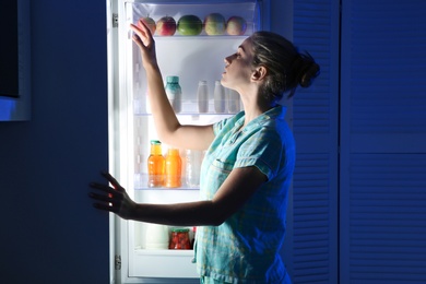 Woman choosing food from refrigerator in kitchen at night