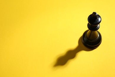 Photo of Black wooden chess king on yellow background, above view. Space for text