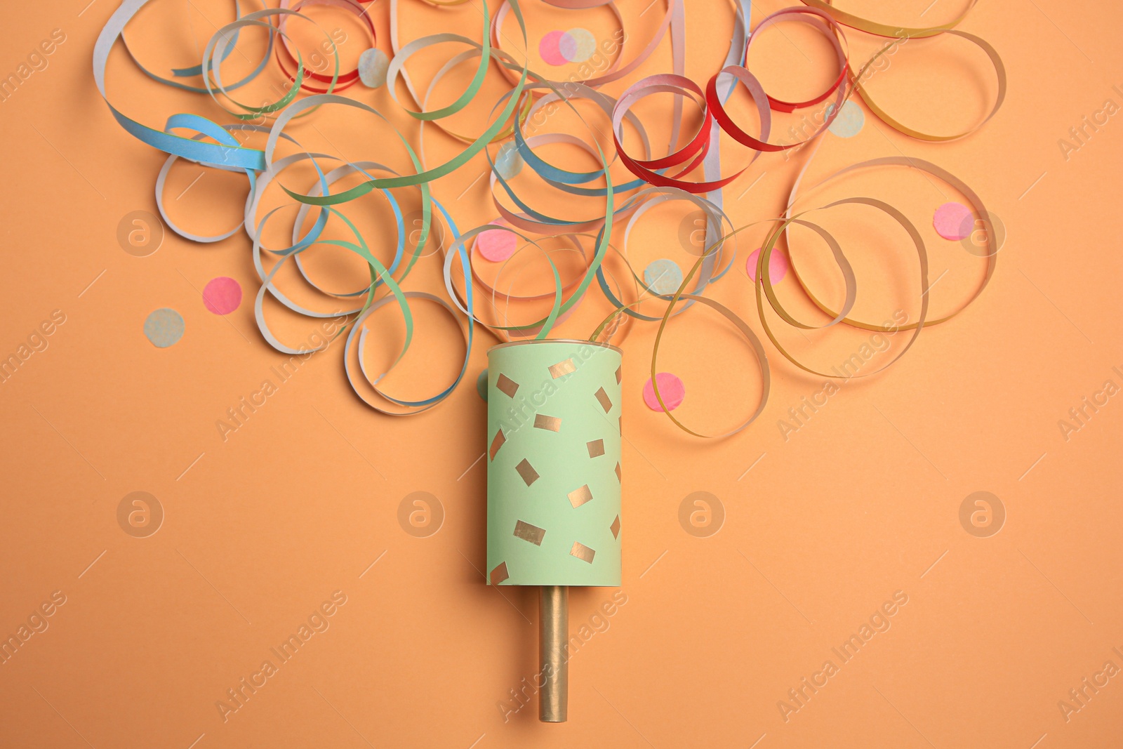 Photo of Beautiful serpentine and confetti bursting out of party popper on coral background, flat lay