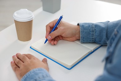 Photo of Young man writing in notebook at white table, closeup