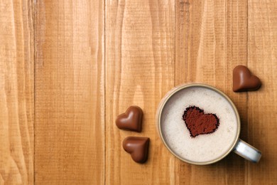 Cup of aromatic coffee with heart shaped decoration and chocolate candies on wooden table, flat lay. Space for text