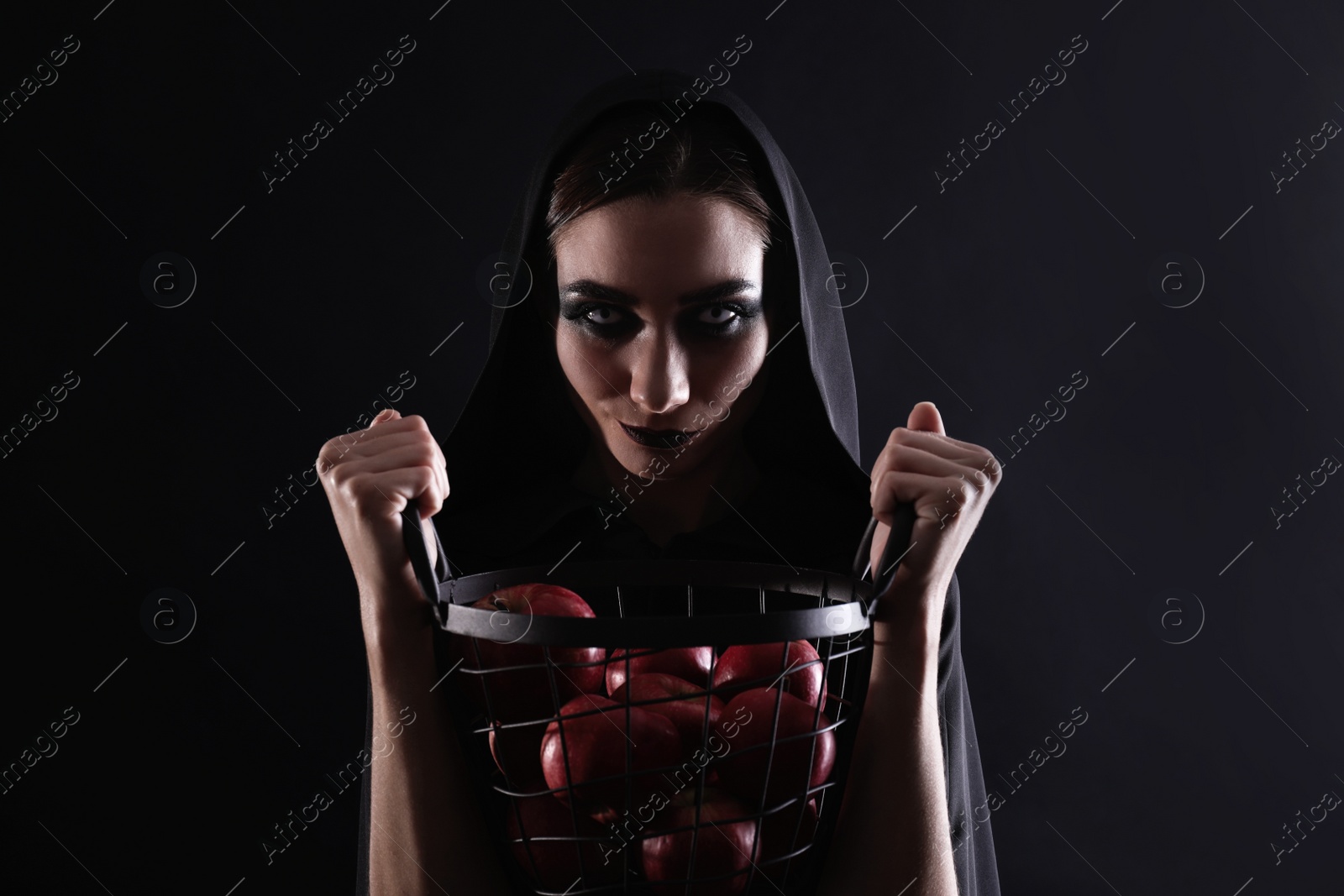 Photo of Mysterious witch with basket full of apples on black background