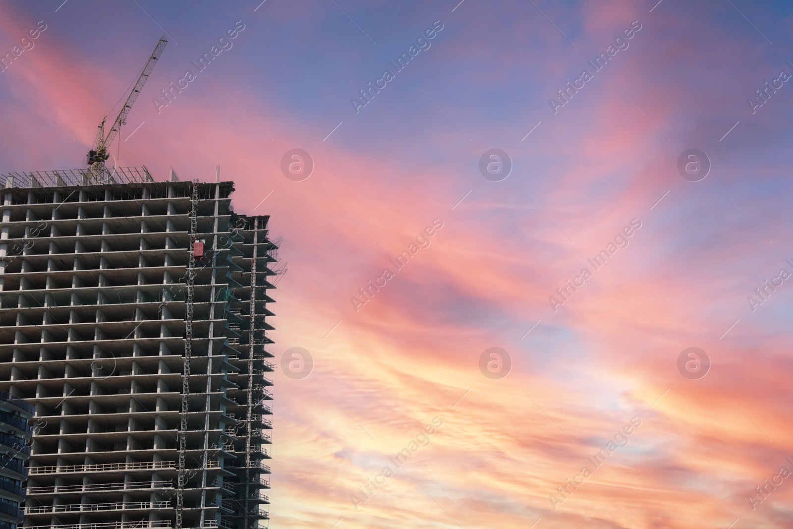 Photo of Construction site with tower crane near unfinished building at sunset, space for text