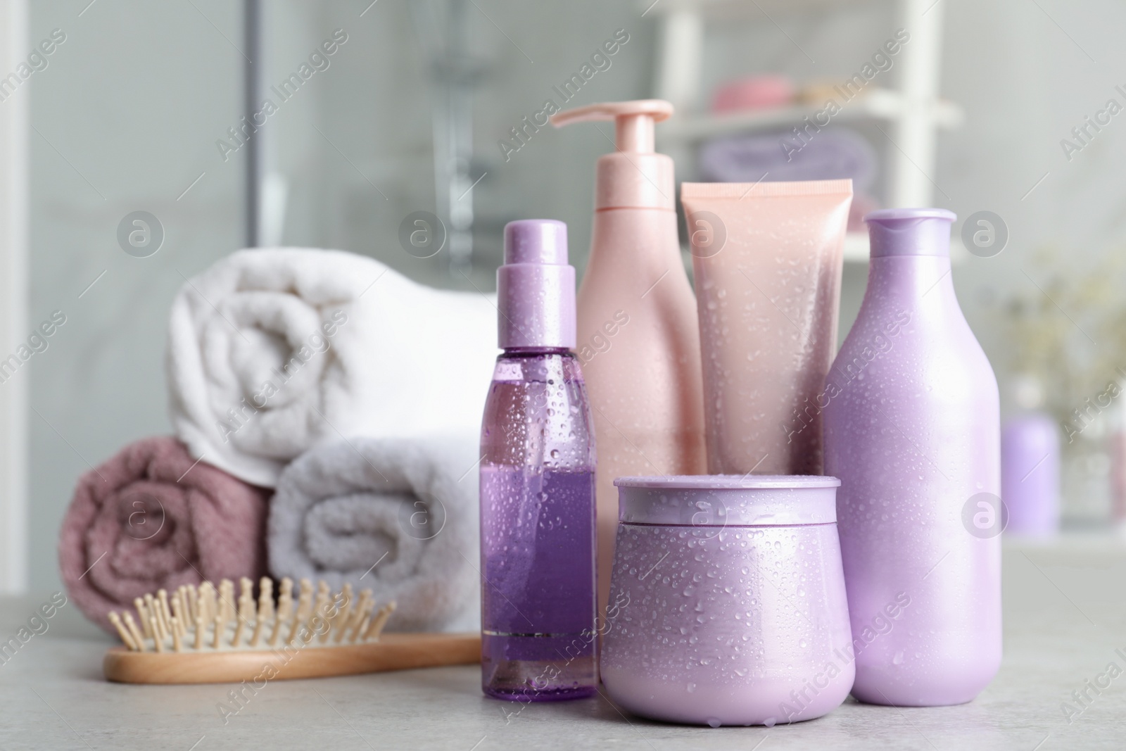 Photo of Set of hair care cosmetic products covered with water drops on light grey stone table in bathroom