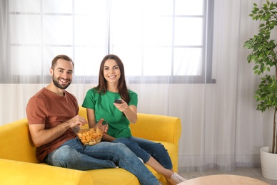 Photo of Young couple watching TV on sofa at home. Space for text