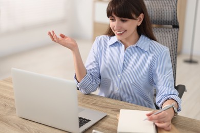 Woman taking notes during webinar at wooden table indoors