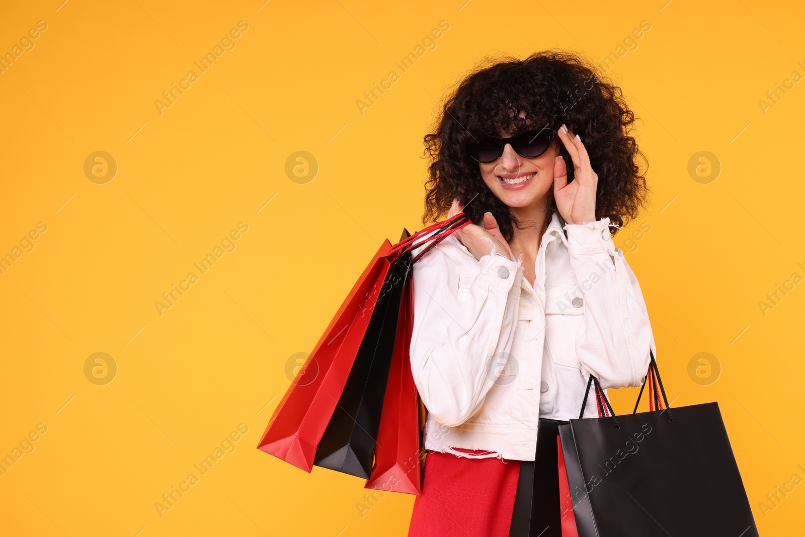 Photo of Happy young woman with shopping bags and stylish sunglasses on yellow background. Space for text