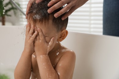 Photo of Mother washing her little son's hair from shampoo in bathroom, closeup