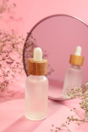Bottle of face serum and beautiful flowers near mirror on pink background