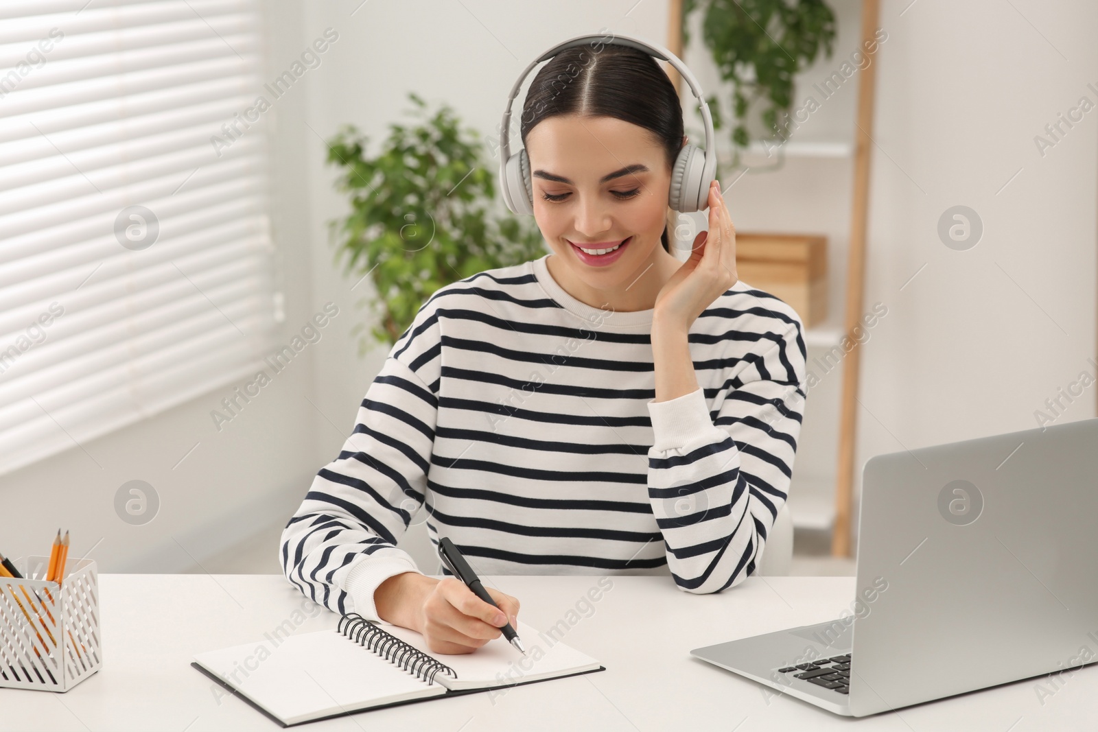 Photo of Online translation course. Student in headphones writing near laptop at home