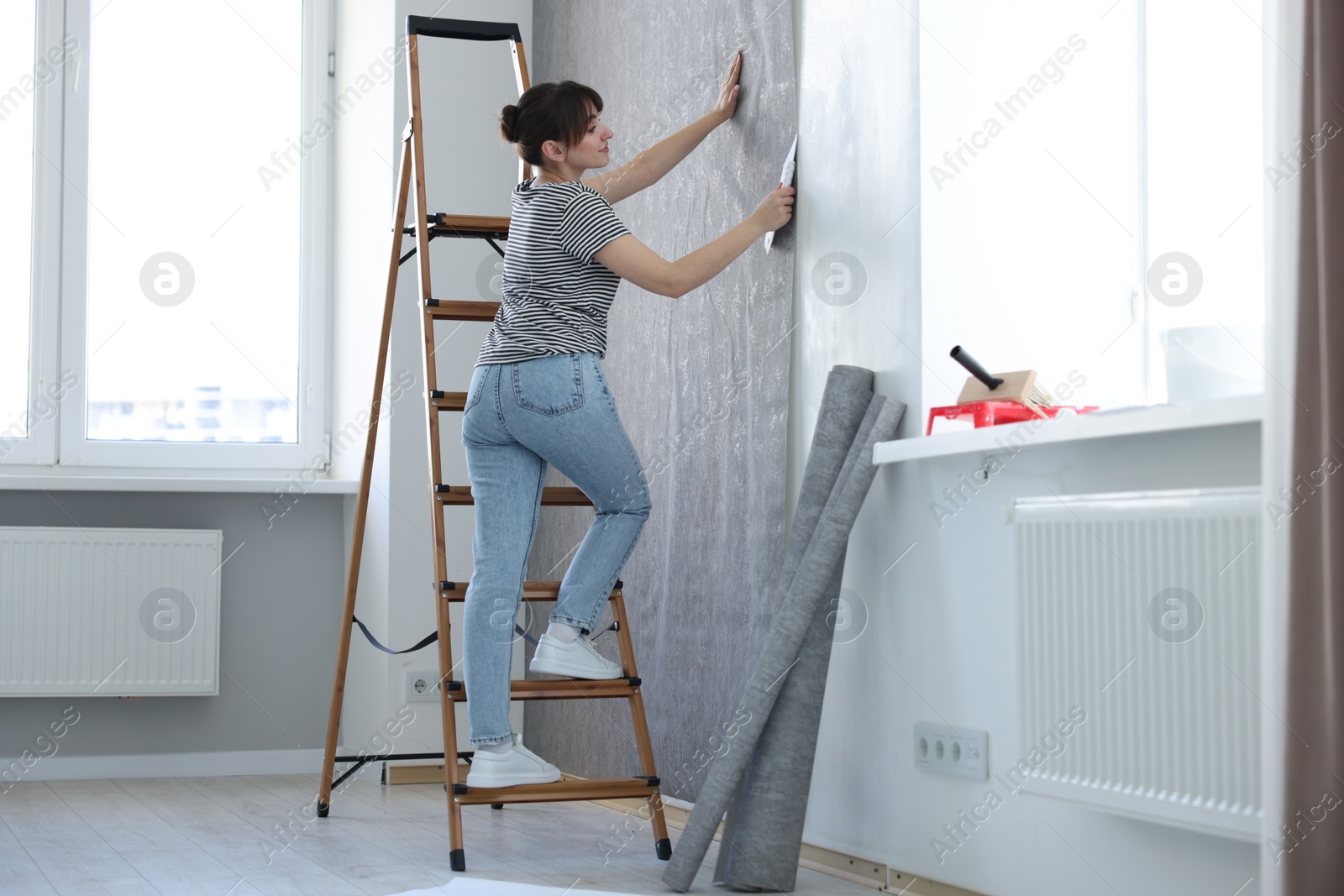 Photo of Woman smoothing stylish gray wallpaper in room