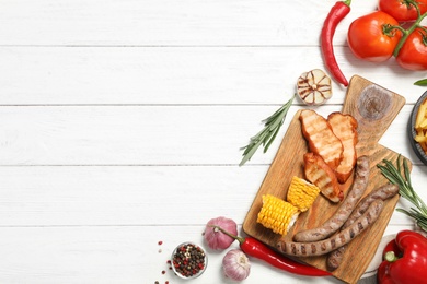 Flat lay composition with barbecued meat and vegetables on white wooden table. Space for text