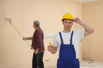 Photo of Worker holding paint roller in unfinished room. Painting walls