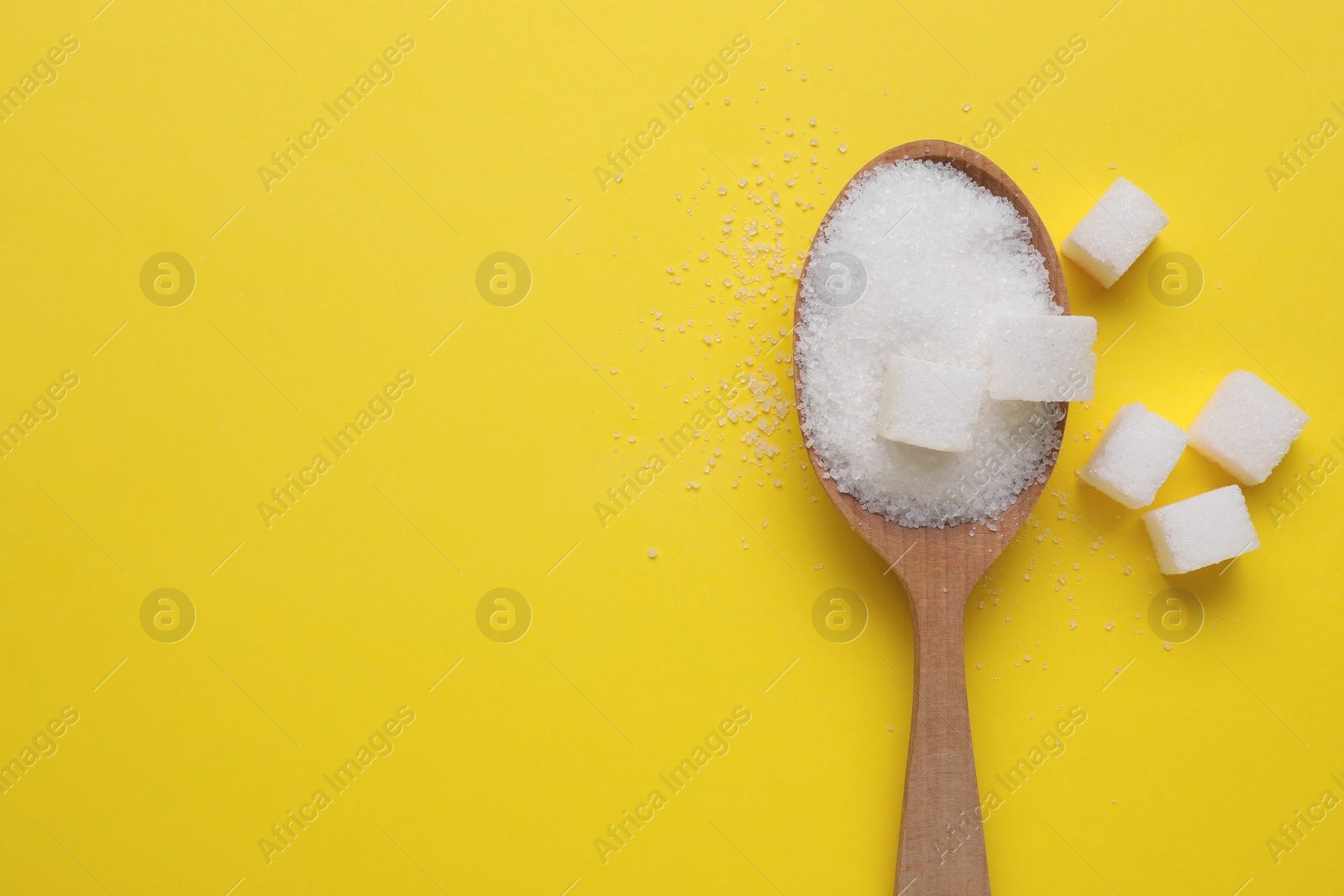 Photo of Spoon with refined and granulated white sugar on yellow background, flat lay. Space for text