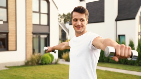 Photo of Sporty man doing exercise with dumbbells on backyard. Healthy lifestyle