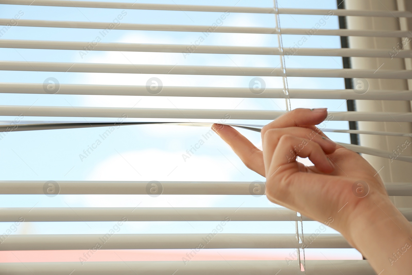 Photo of Woman opening horizontal window blinds at home, closeup. Space for text