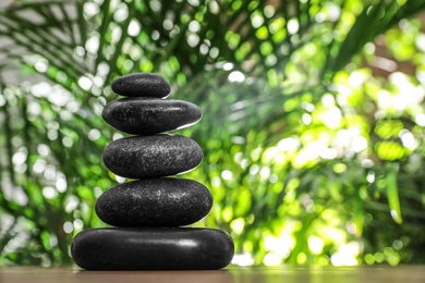 Table with stack of stones and blurred green leaves on background, space for text. Zen concept