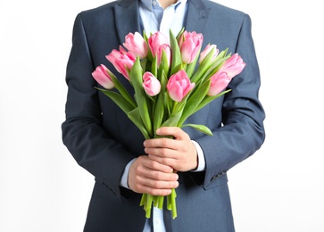 Man in elegant suit holding bouquet of beautiful spring tulips on light background, closeup. International Women's Day