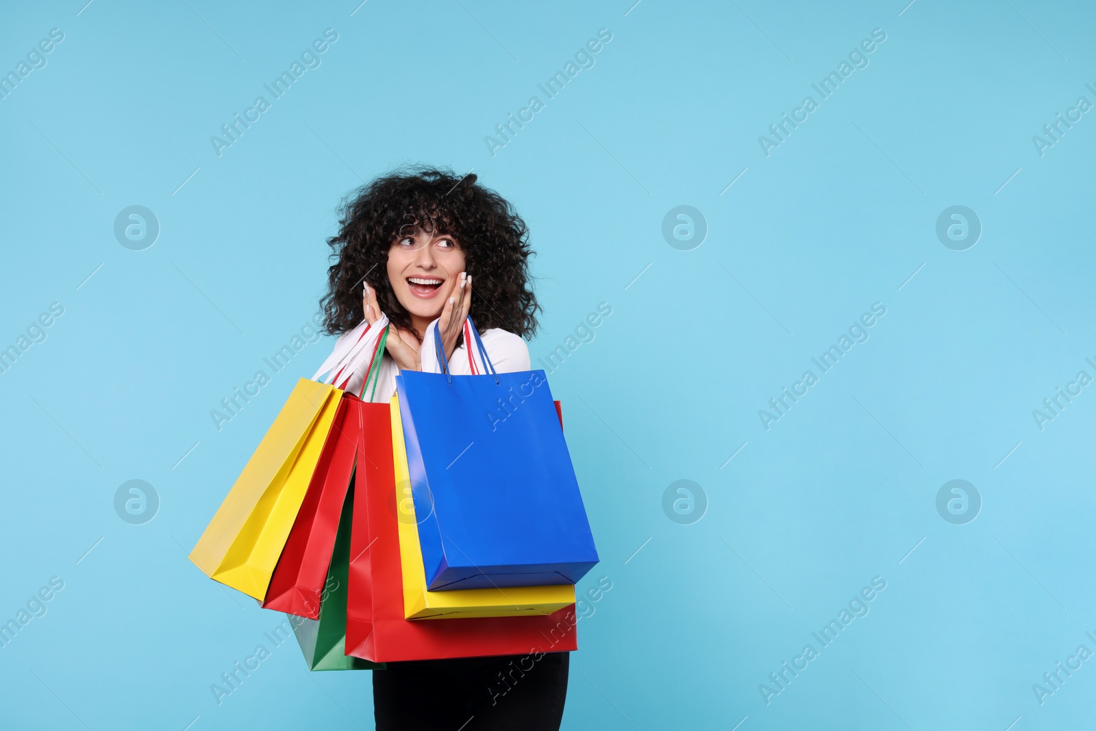 Photo of Happy young woman with shopping bags on light blue background. Space for text